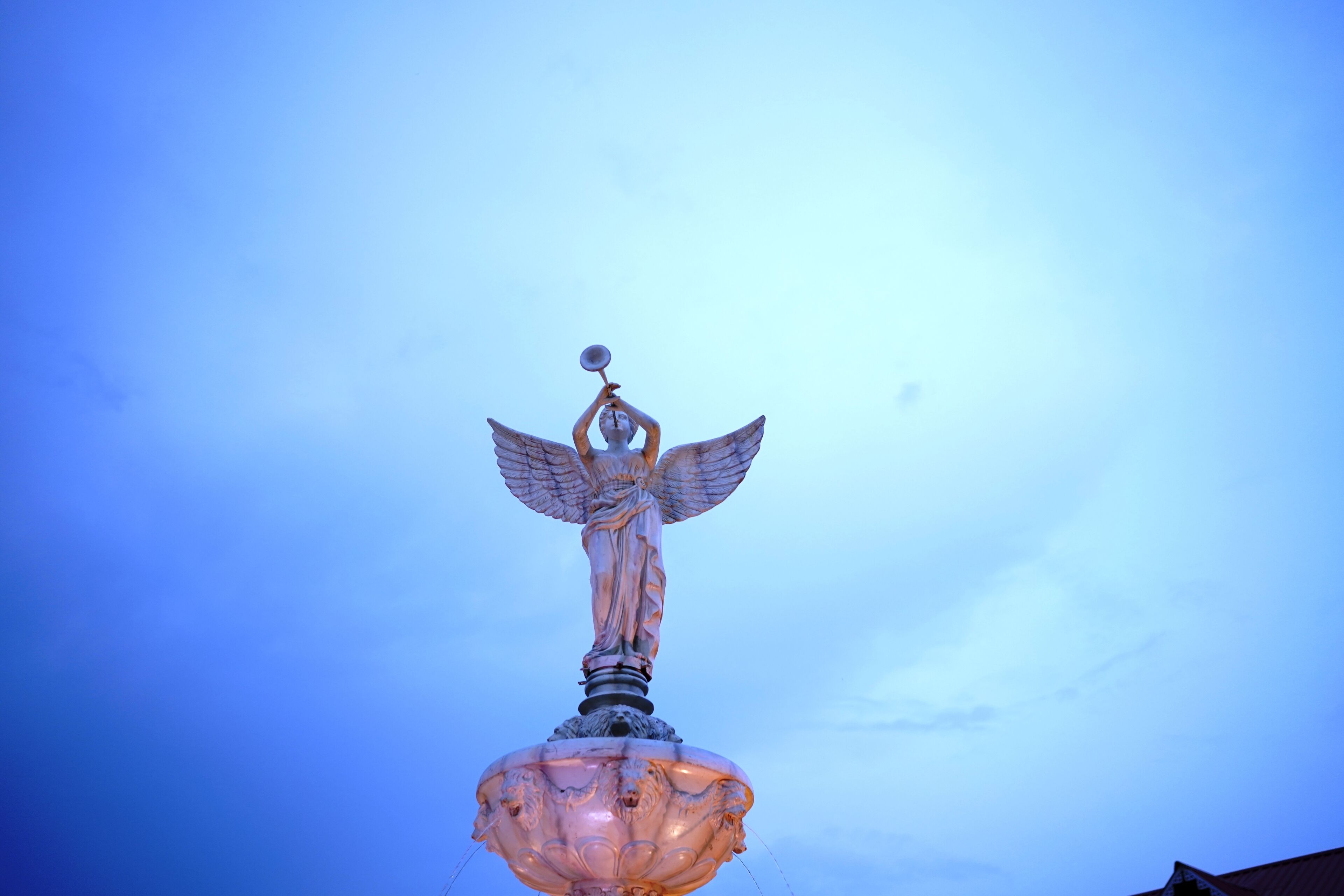 A statue of an angel with wings on a pedestal, set against a clear sky.