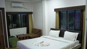 Une chambre d’hôtel avec un lit, un fauteuil vert, une petite table et une fenêtre avec des rideaux.