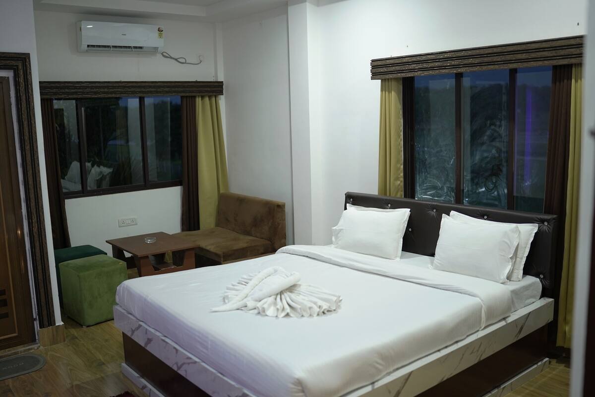 A hotel room with a bed, a green chair, a small table, and a window with curtains.