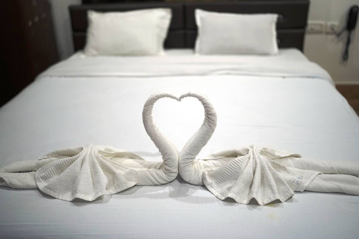 A neatly made bed with a heart-shaped towel arrangement on the bedspread.