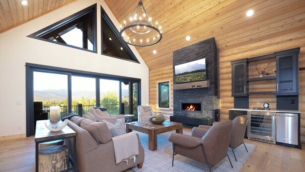 A modern log cabin interior with a fireplace, large windows, and a cozy seating area.