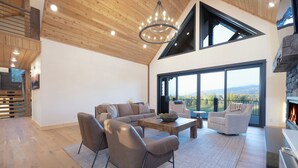 A spacious living area with a high ceiling, a large window offering a view of the outdoors, and a fireplace.