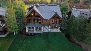 A large, multi-story log cabin with a stone foundation, multiple balconies, and a spacious interior visible through the windows.