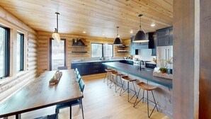 A modern log cabin kitchen with a central island, bar stools, and pendant lighting.