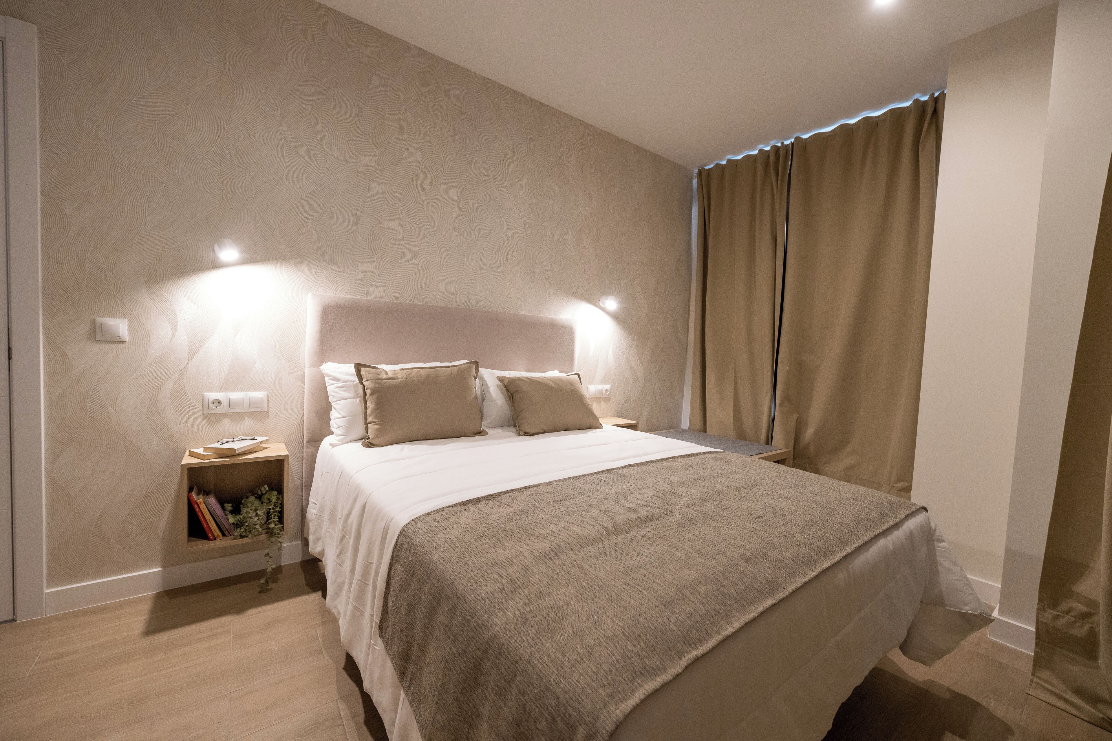 A neatly arranged bedroom with a large bed, bedside lamps, and a nightstand with books.