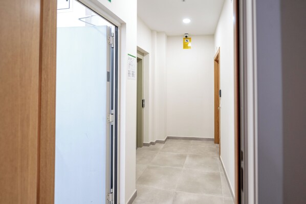 Un pasillo con una puerta a la izquierda, una lámpara en el techo y otra puerta a la derecha.