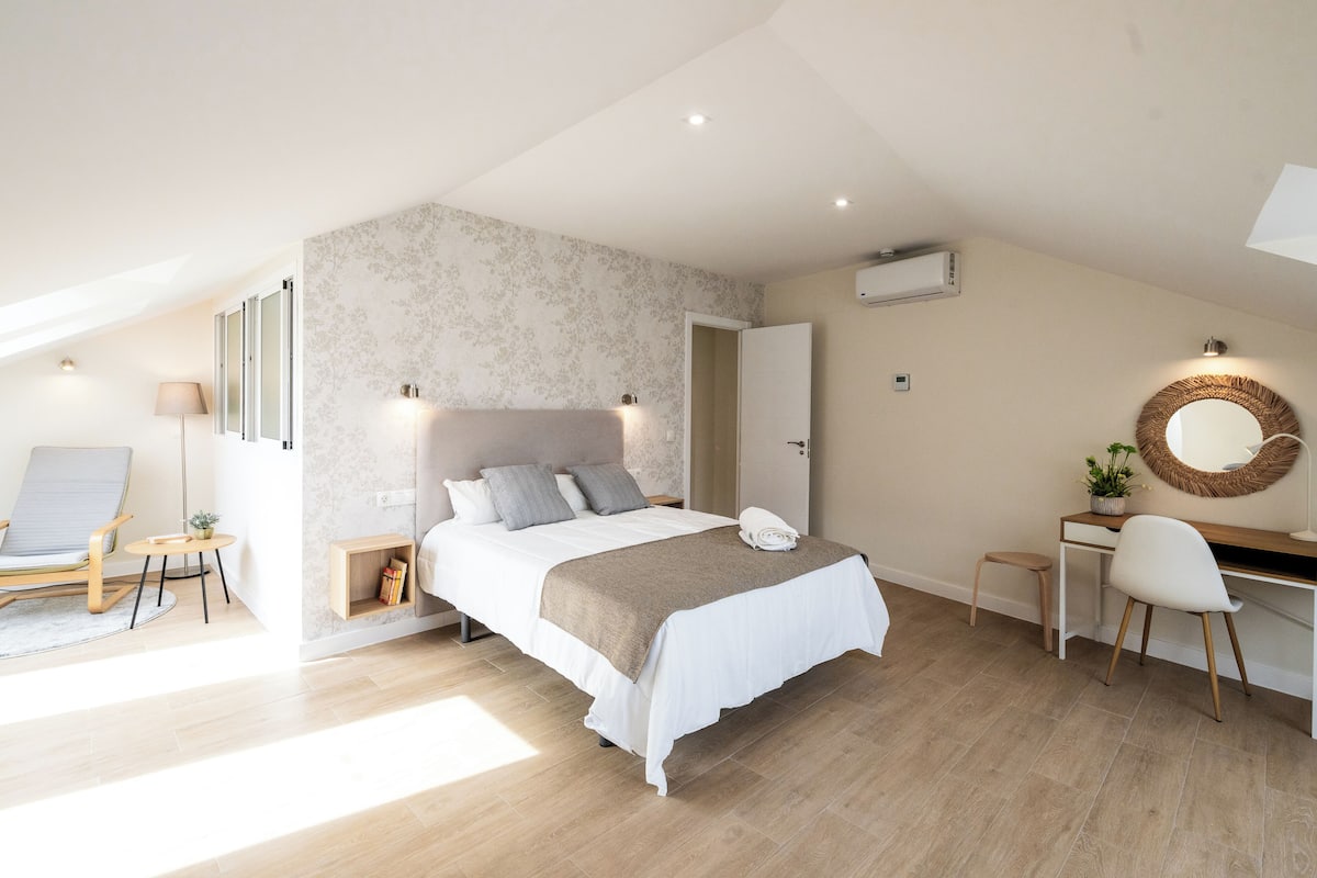 A bedroom with a bed, a desk, a chair, and a small stool.