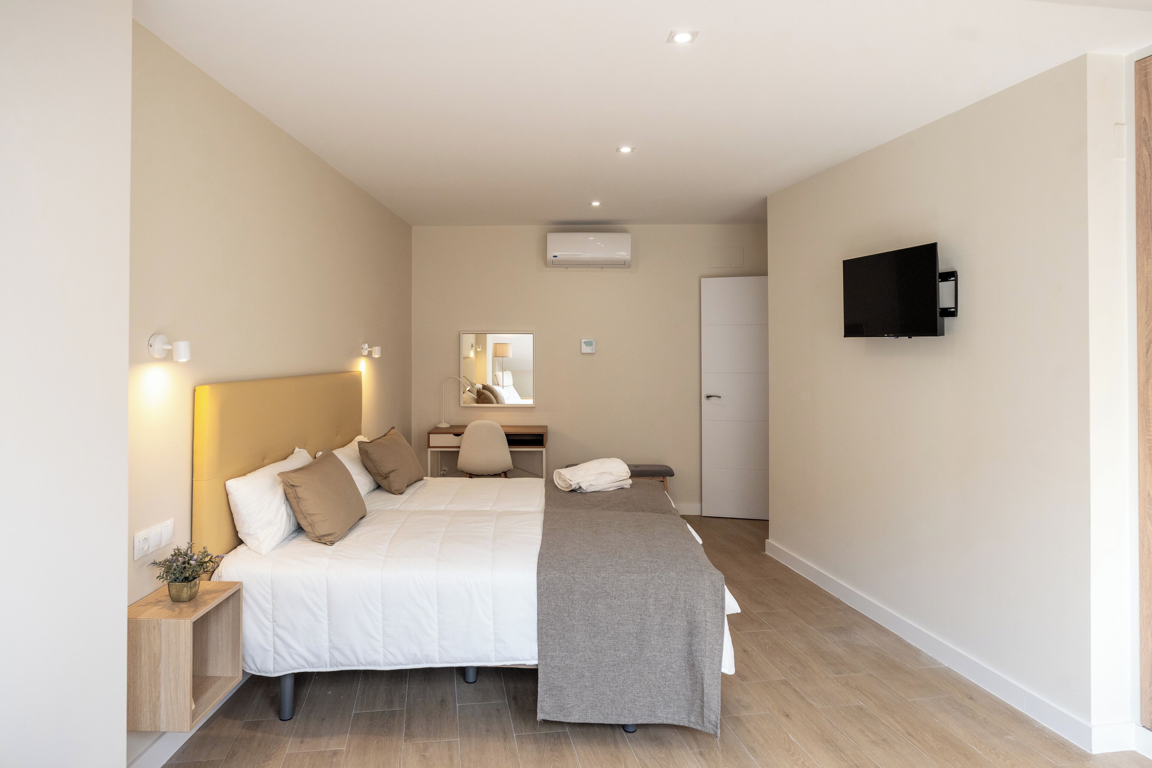 Une chambre à coucher comprenant un lit, une table de chevet, un bureau, une chaise et un téléviseur fixé au mur.