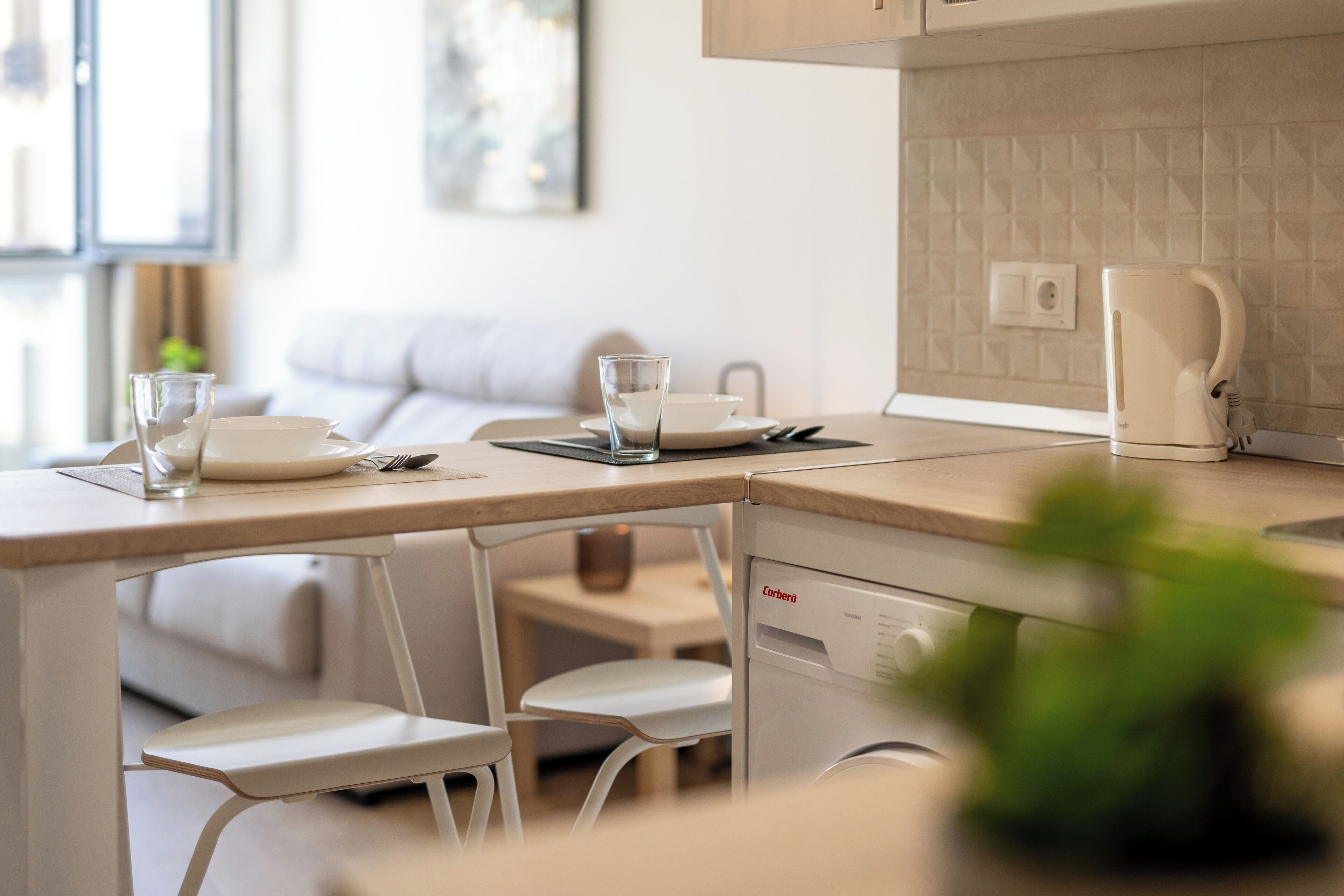 A modern kitchen with a dishwasher, a coffee maker, and a dining area with a table set for two.