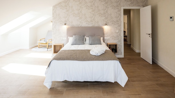 Ein Schlafzimmer mit einem großen Bett, einem Kopfteil, Nachttischen und einer Tür zu einem anderen Raum.