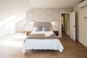 Un dormitorio con una cama grande, cabecera, mesitas de noche y una puerta que da a otra habitación.