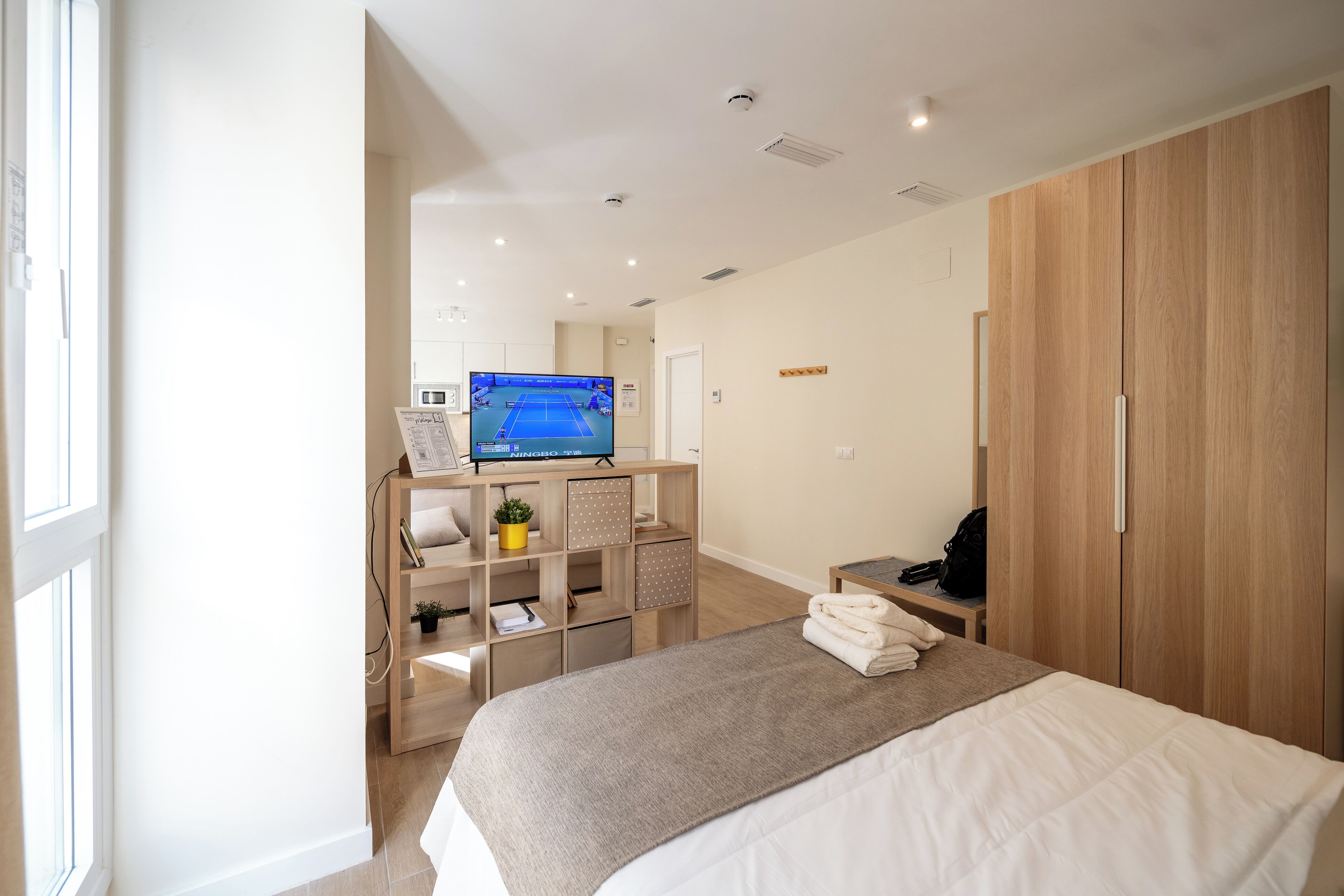 Una habitación de hotel moderna con una cama grande, un televisor, un armario de madera y un escritorio con una silla.