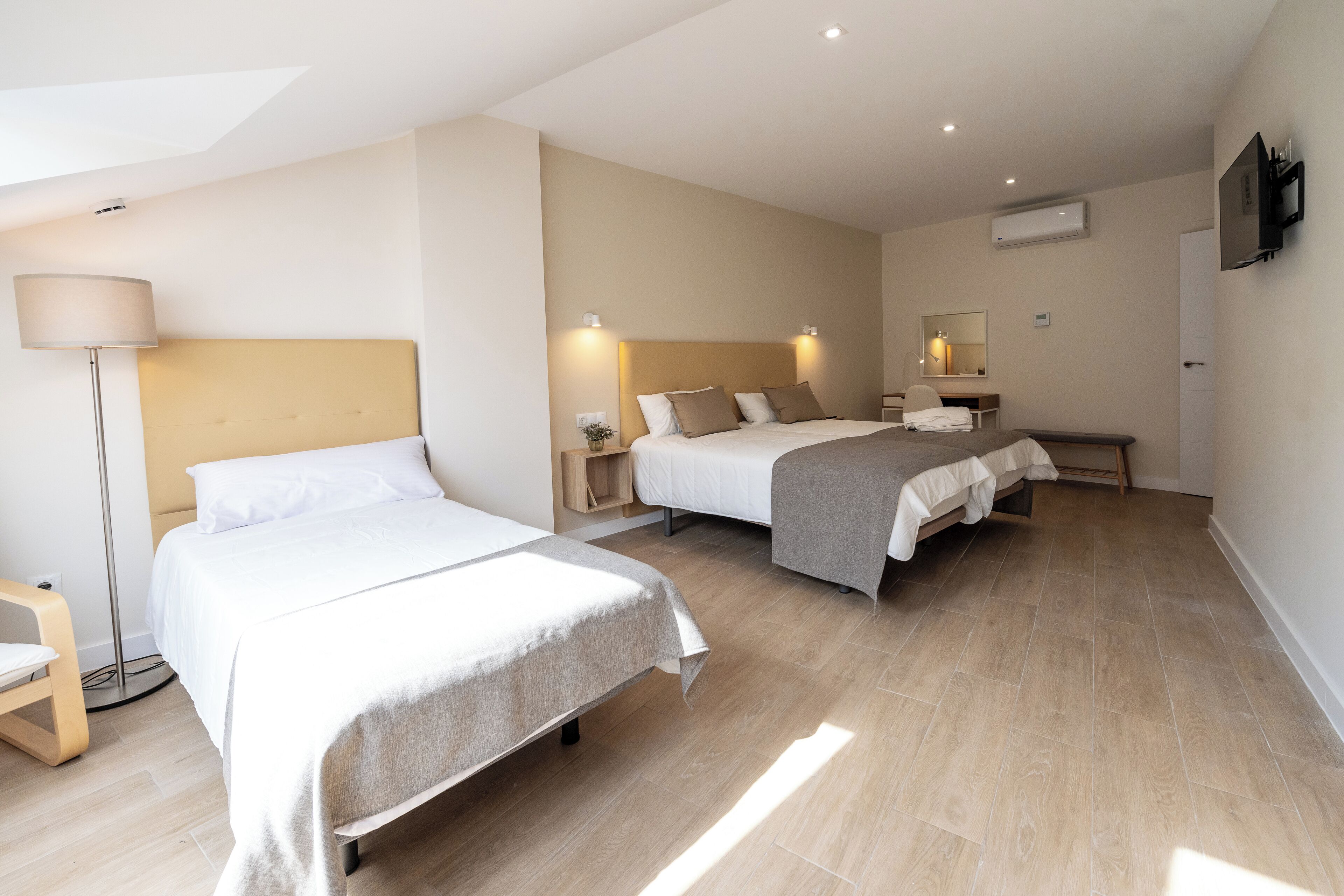 A hotel room with two beds, a desk, a chair, a lamp, and a TV.