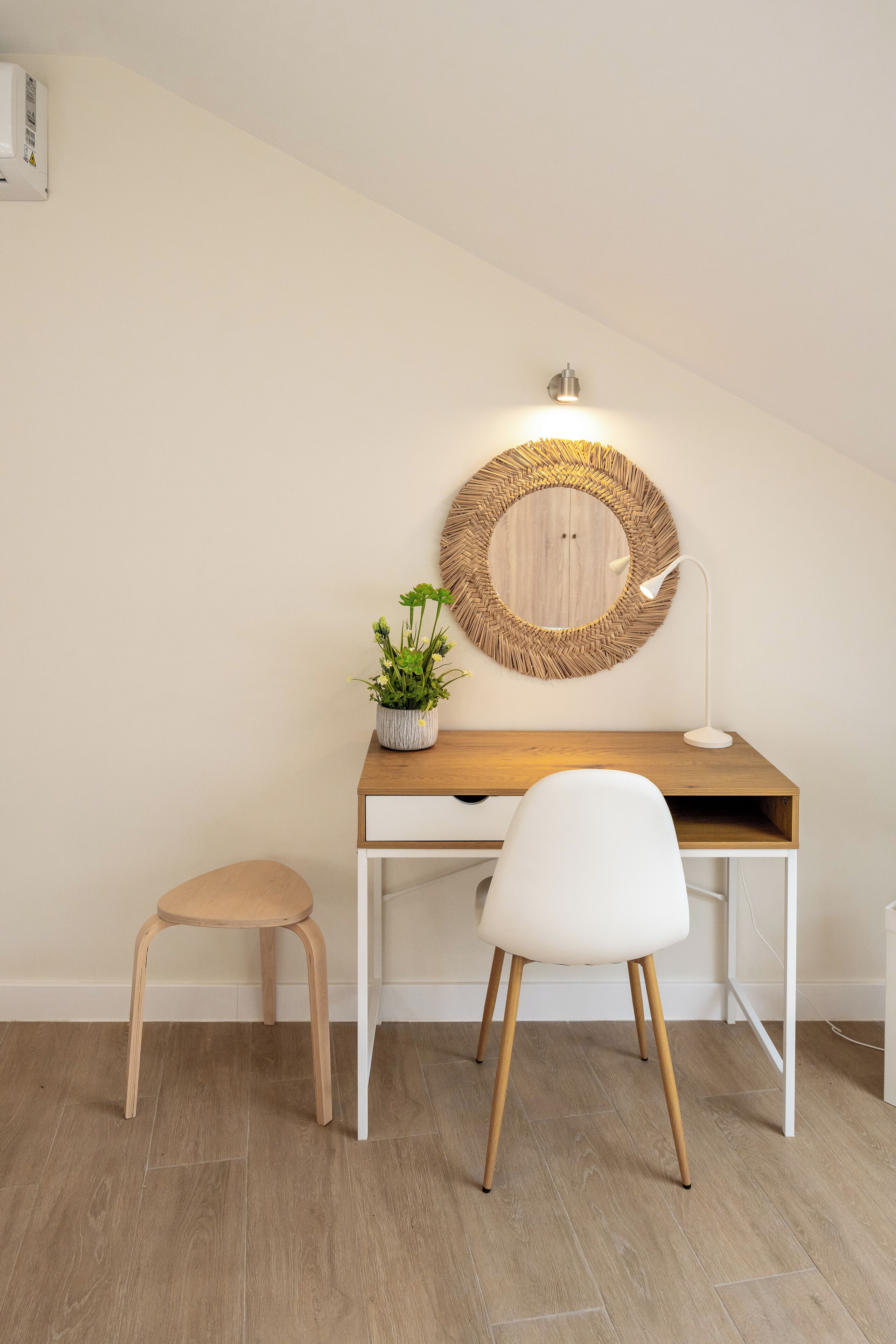 A modern desk with a round mirror, a small potted plant, and a white chair.