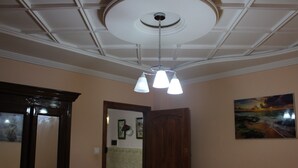 Een kamer met een plafondventilator, een houten deur, een lijst met een afbeelding aan de muur, en een lamp met drie lampen.