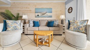 Ein Wohnzimmer mit einer Holzwand, einem Sofa, zwei Sesseln, einem Couchtisch und einem Bild eines Bootes an der Wand.