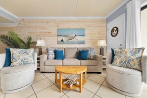 A living room with a wooden wall, a sofa, two armchairs, a coffee table, and a painting of a boat on the wall.