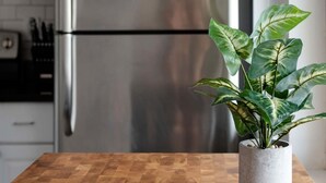 Una cocina con un refrigerador de acero inoxidable, un microondas y una planta en maceta sobre una mesa de madera.