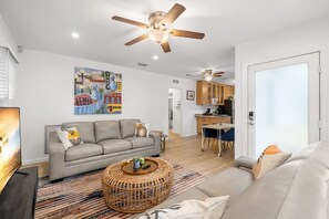 Relax in this stylish living room with a sofa, coffee table, and large painting, plus a kitchen area with dining table.