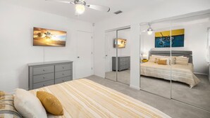 Un dormitorio con una cama, un aparador, un armario, un ventilador de techo y dos cuadros en la pared.