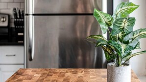 Una cocina con un refrigerador de acero inoxidable, un microondas y una planta en maceta sobre una mesa de madera.