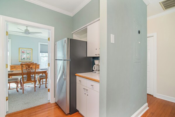 A kitchen with a refrigerator, cabinets, and a dining area with chairs and a table.