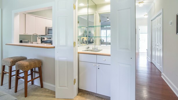A kitchen with white cabinets, a glass backsplash, and a microwave. There are two wicker stools and a white door leading to another room.