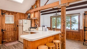 A rustic kitchen with wooden walls, a white countertop, and a bar area with stools.