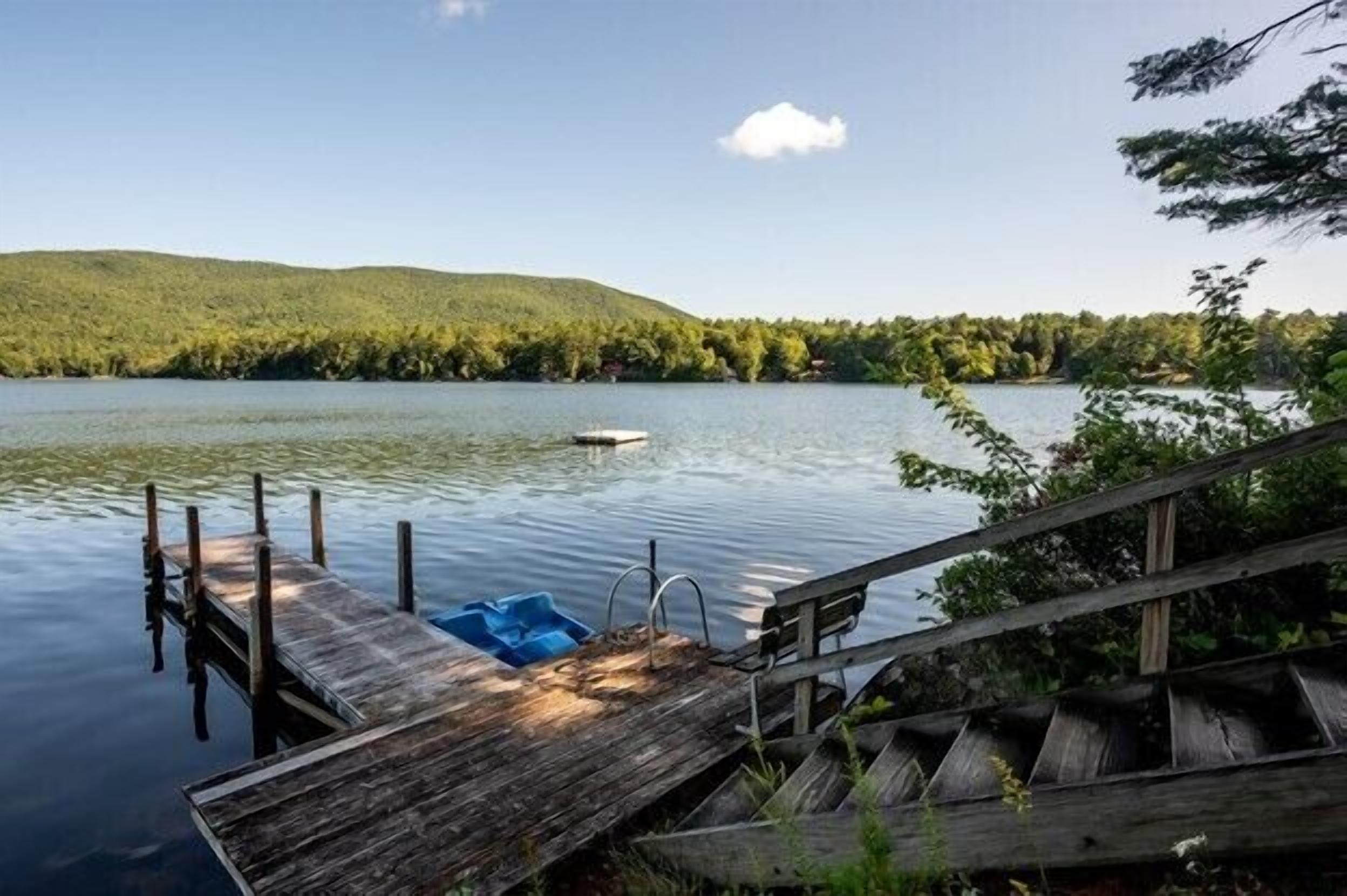 A wooden dock extending into calm water with a small boat and a blue container on it.
