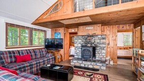 A cozy cabin interior with a stone fireplace, a plaid sofa, and a television.