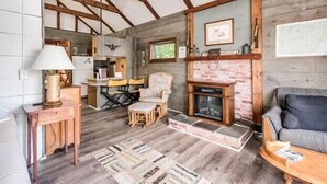 A rustic interior with exposed wooden beams, a fireplace, a sofa, and a dining area. - Charming boathouse for two with deck overlooking Lake Kanasatka (Moultonborough)