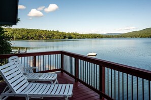 Una terraza con sillones blancos que da a un lago tranquilo, rodeada de abundante vegetación y colinas a lo lejos.