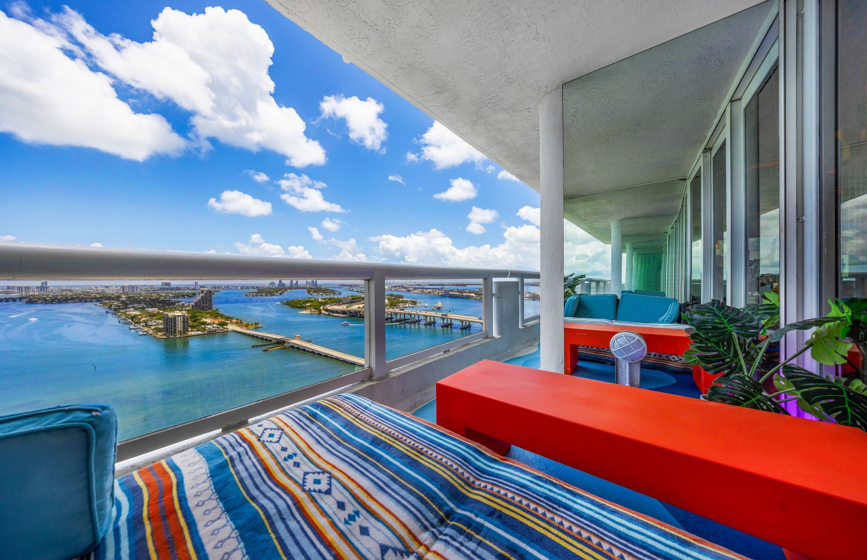 A balcony with a view of a marina and city skyline, featuring a red sofa and patterned cushions.