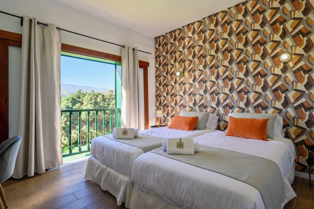 Een hotelkamer met twee bedden, een balkon met gordijnen en een behang met patroon.
