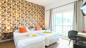 Ein Hotelzimmer mit zwei Betten, einer Wand mit Muster, einem Balkon mit Blick und einem Schreibtisch mit Stuhl.