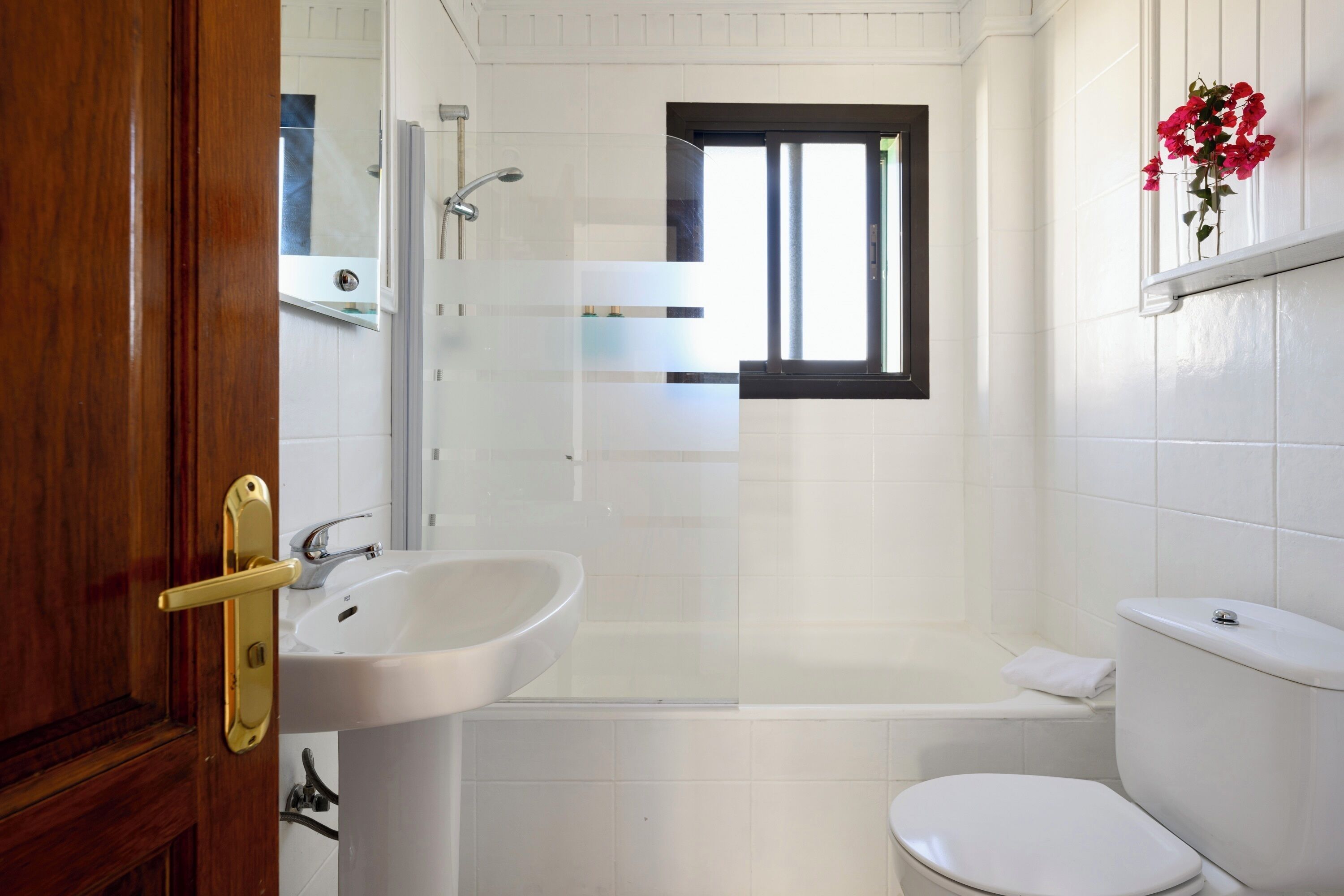 Een badkamer met een wit wastafel, toilet, douche en raam.