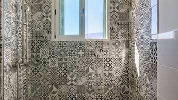 Een badkamer met patroontegels, een douche, een raam en een handdoekrek.
