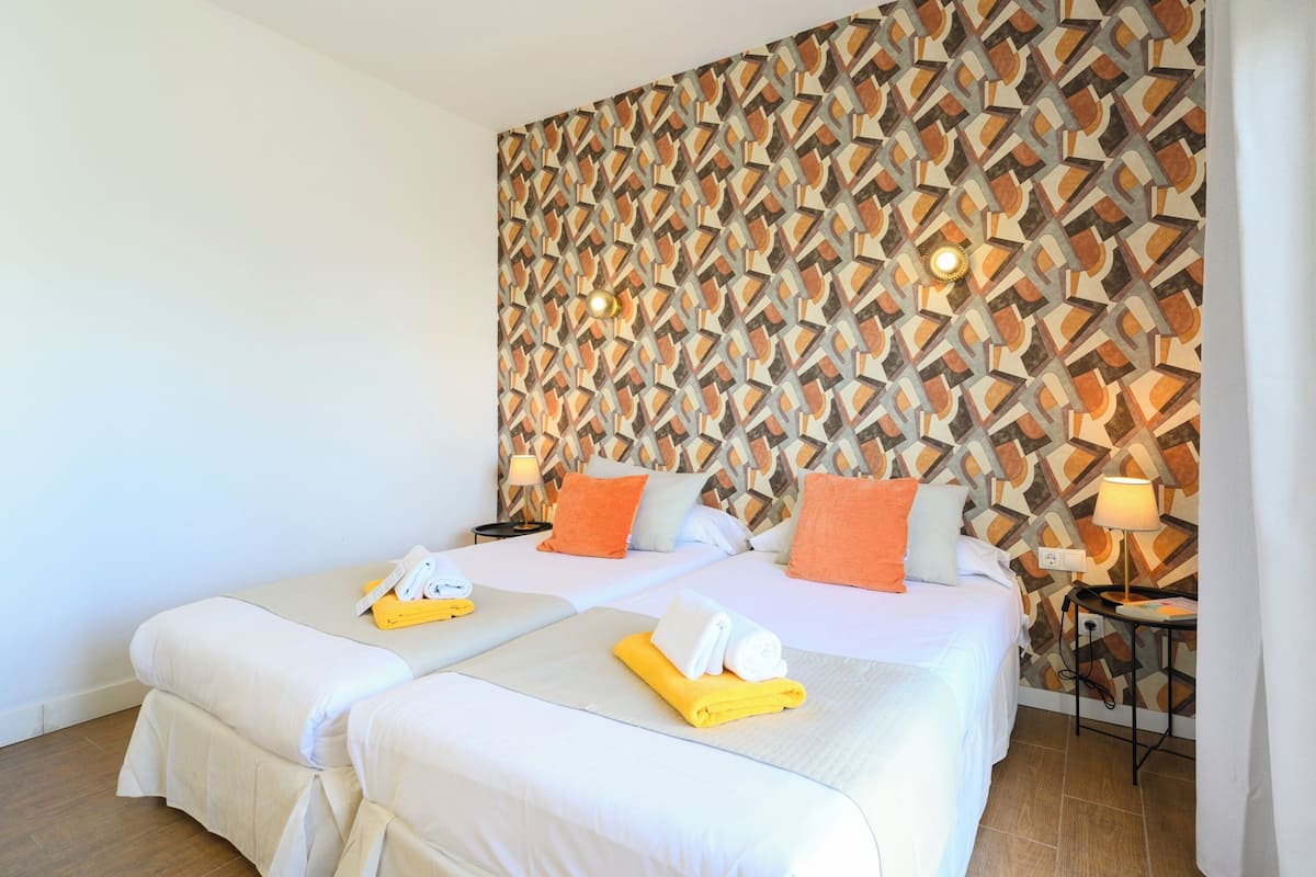 Een hotelkamer met twee bedden, een behang met patroon en een kleine tafel met een lamp.