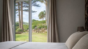 A bedroom with a large bed, a view of a landscaped garden, and a stone wall. - Bandama Golf Hotel by Airnest (Santa Brigida)