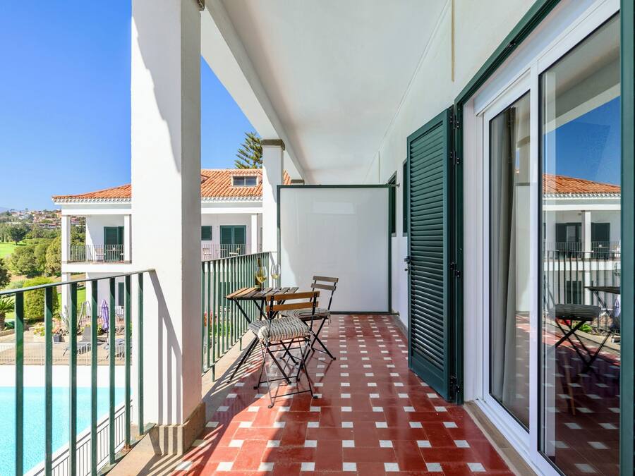 A balcony with a checkered floor, a table with chairs, and a view of neighboring buildings.