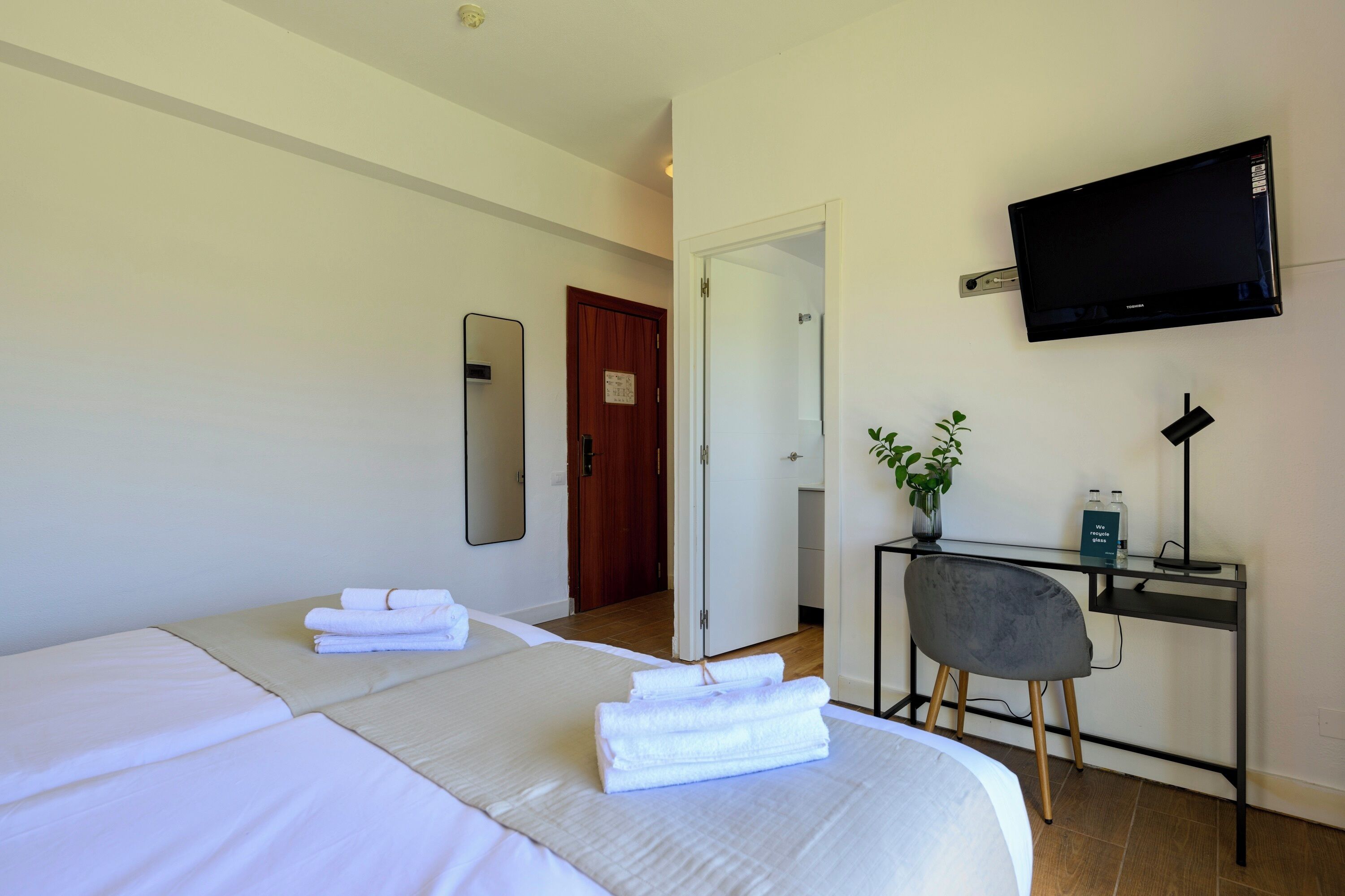Una camera d'albergo con un letto, una scrivania con una sedia, un televisore e una porta che conduce a un'altra stanza.