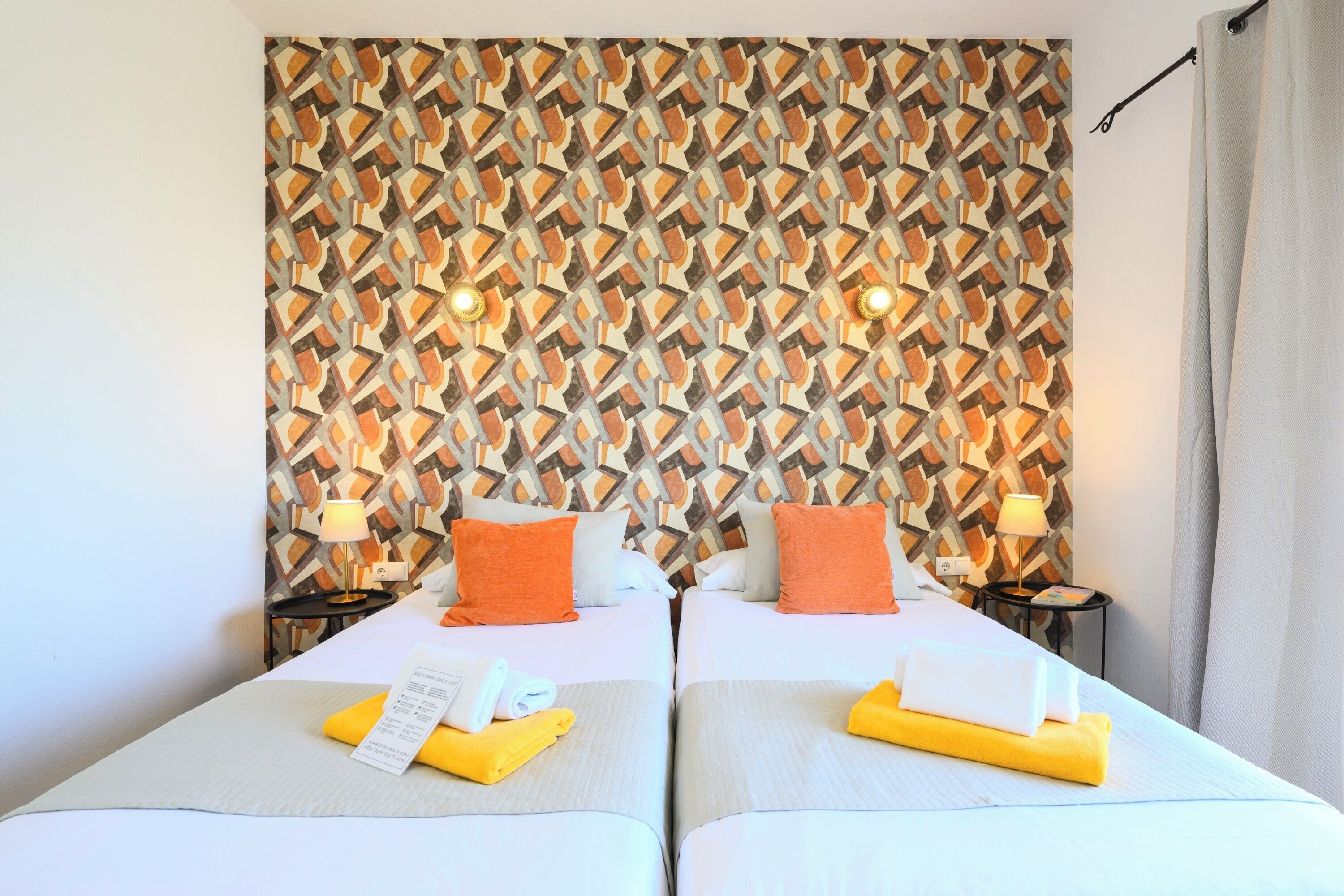 Een hotelkamer met twee bedden, een behang met patroon en een gordijn.