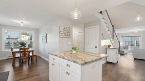 Una cocina moderna con una isla central, mesa de comedor de madera y una escalera que sube a otro nivel.