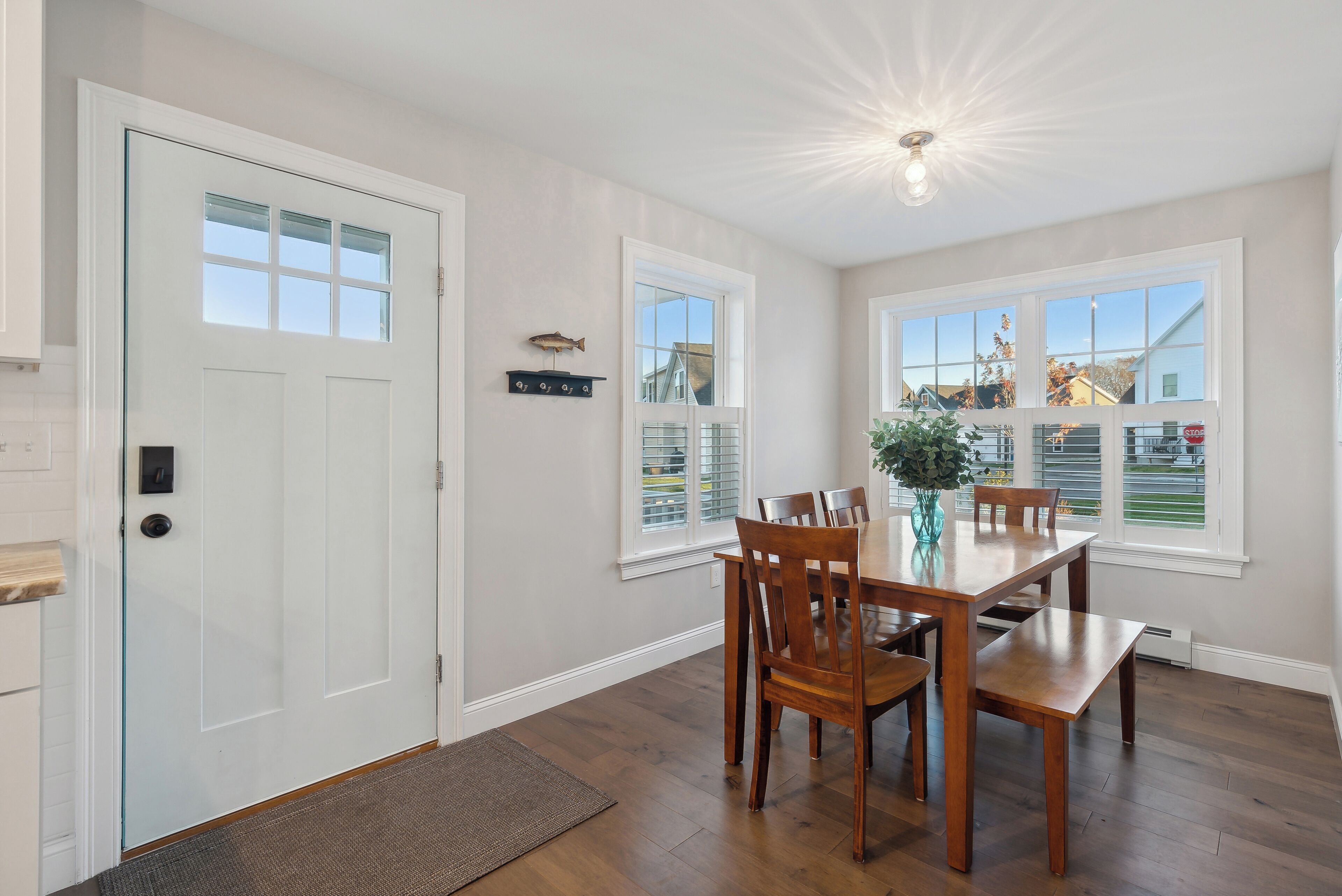 A dining area with a wooden table and chairs, a white door, and windows with blinds.