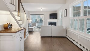 Una sala de estar moderna con una escalera, una chimenea y ventanas grandes.