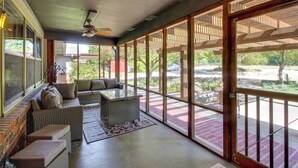 A sunlit room with a large window, a ceiling fan, and a wicker sofa with cushions. - Kansas Gem w/ Fire Pit & Views: 10 Mi to Dtwn! (Manhattan)