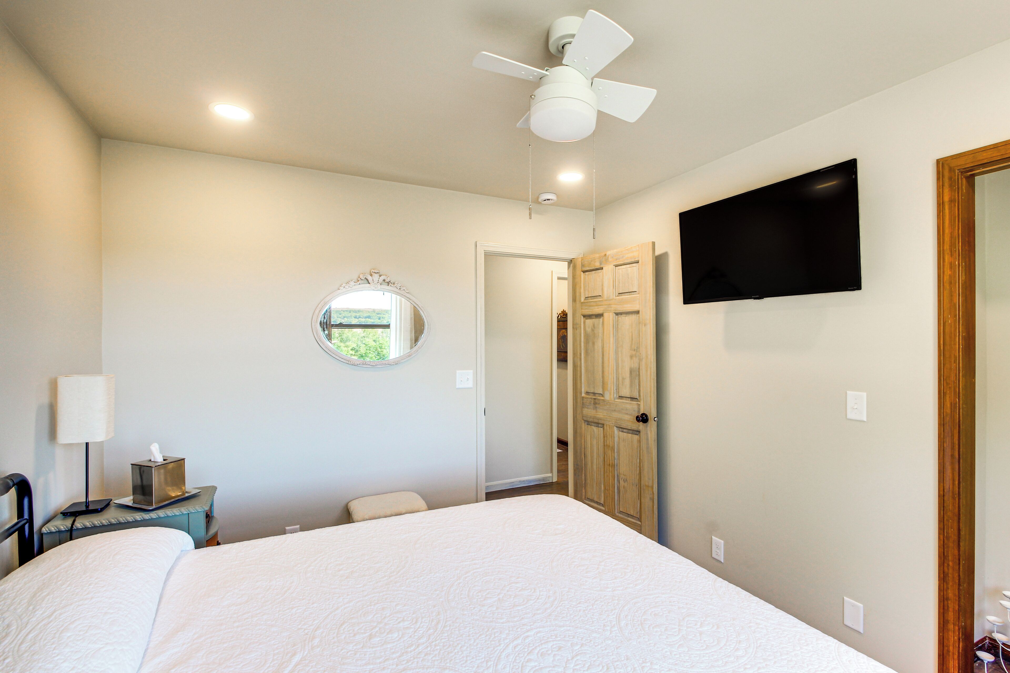 Quarto de hotel com cama, ventoinha no teto, televisão presa na parede e porta de madeira.