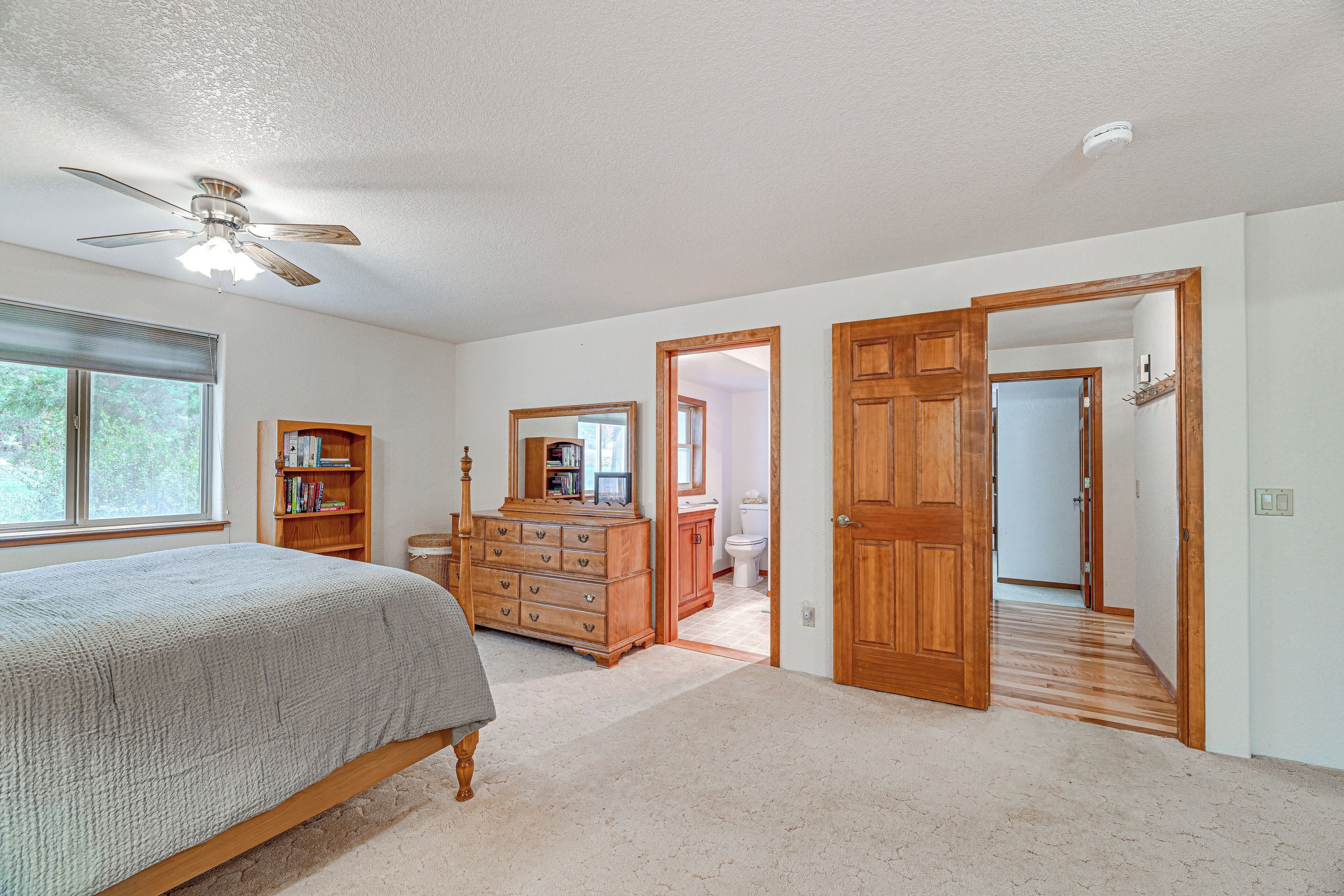 A bedroom with a bed, a dresser, a ceiling fan, and a door leading to another room.