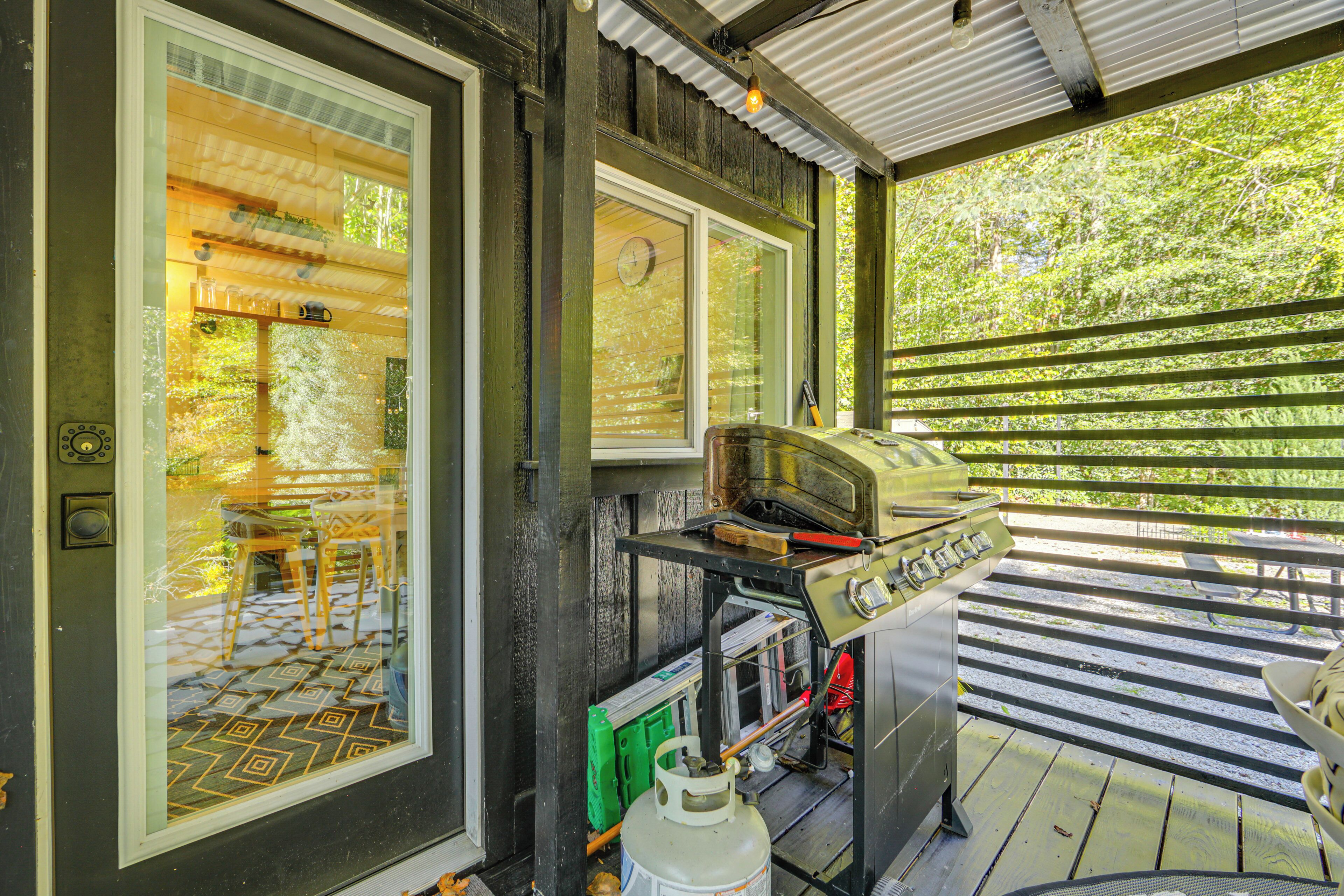 A covered outdoor area with a grill, a table, and a view of the surrounding greenery.