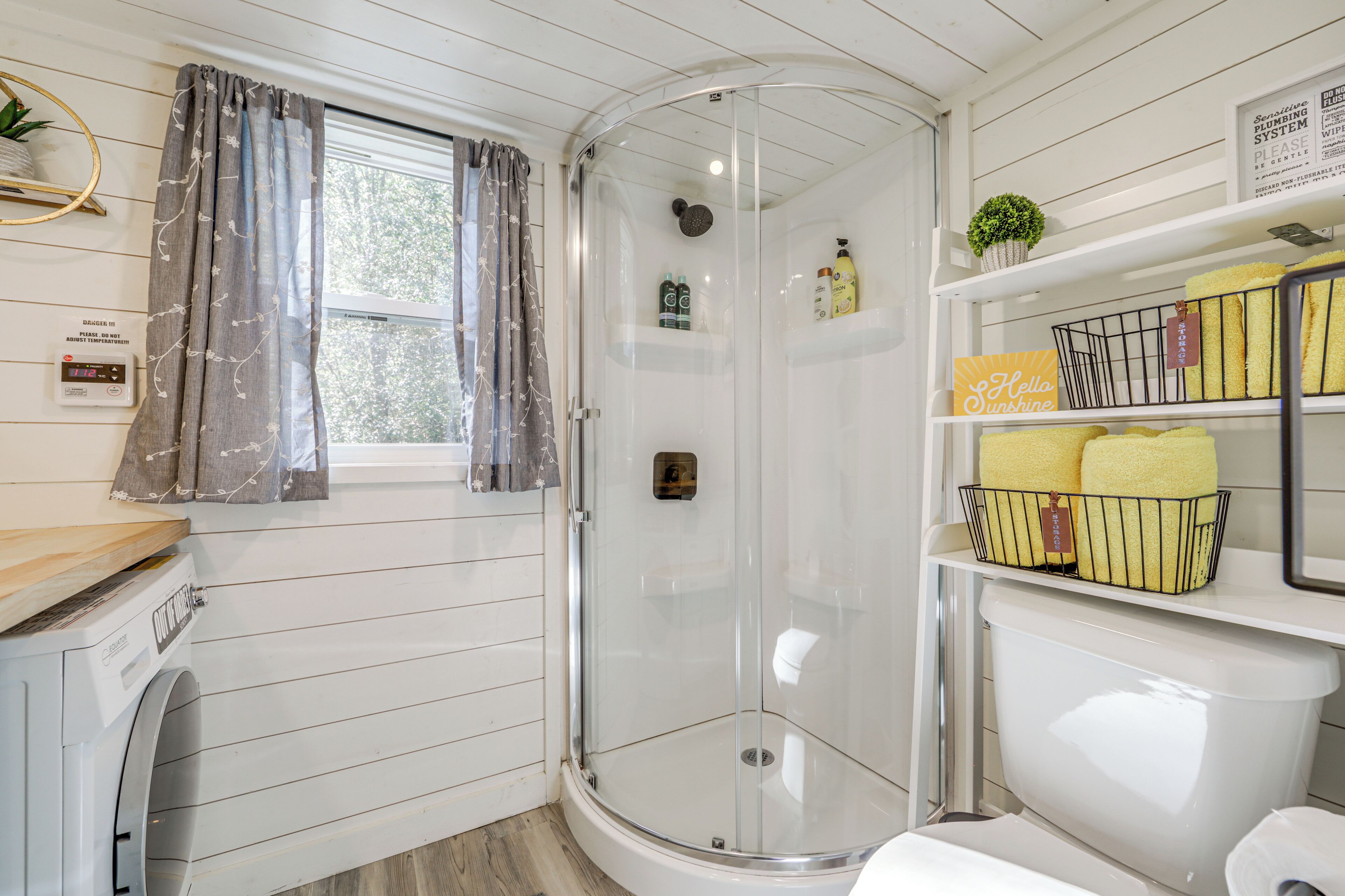 Een badkamer met een douchecabine, een toilet, een wastafel en planken met toiletartikelen.